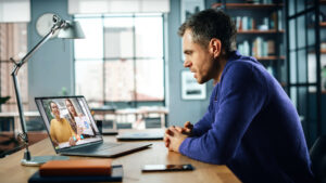 Man sitting at home office on laptop while meeting with financial coach on video call