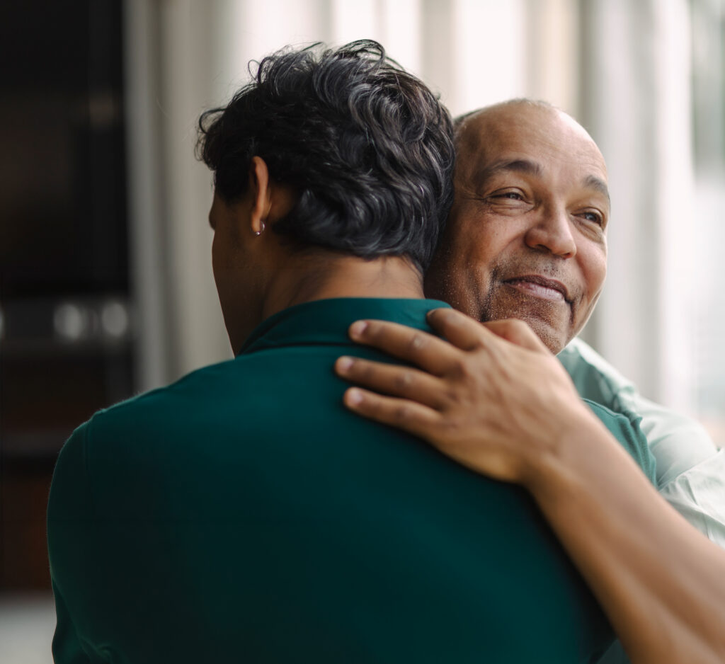 Two men embracing in a hug while smiling. one older than the other.