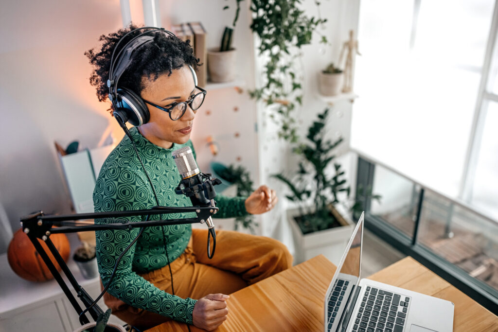 Woman wearing headphones while recording a podcast in home office