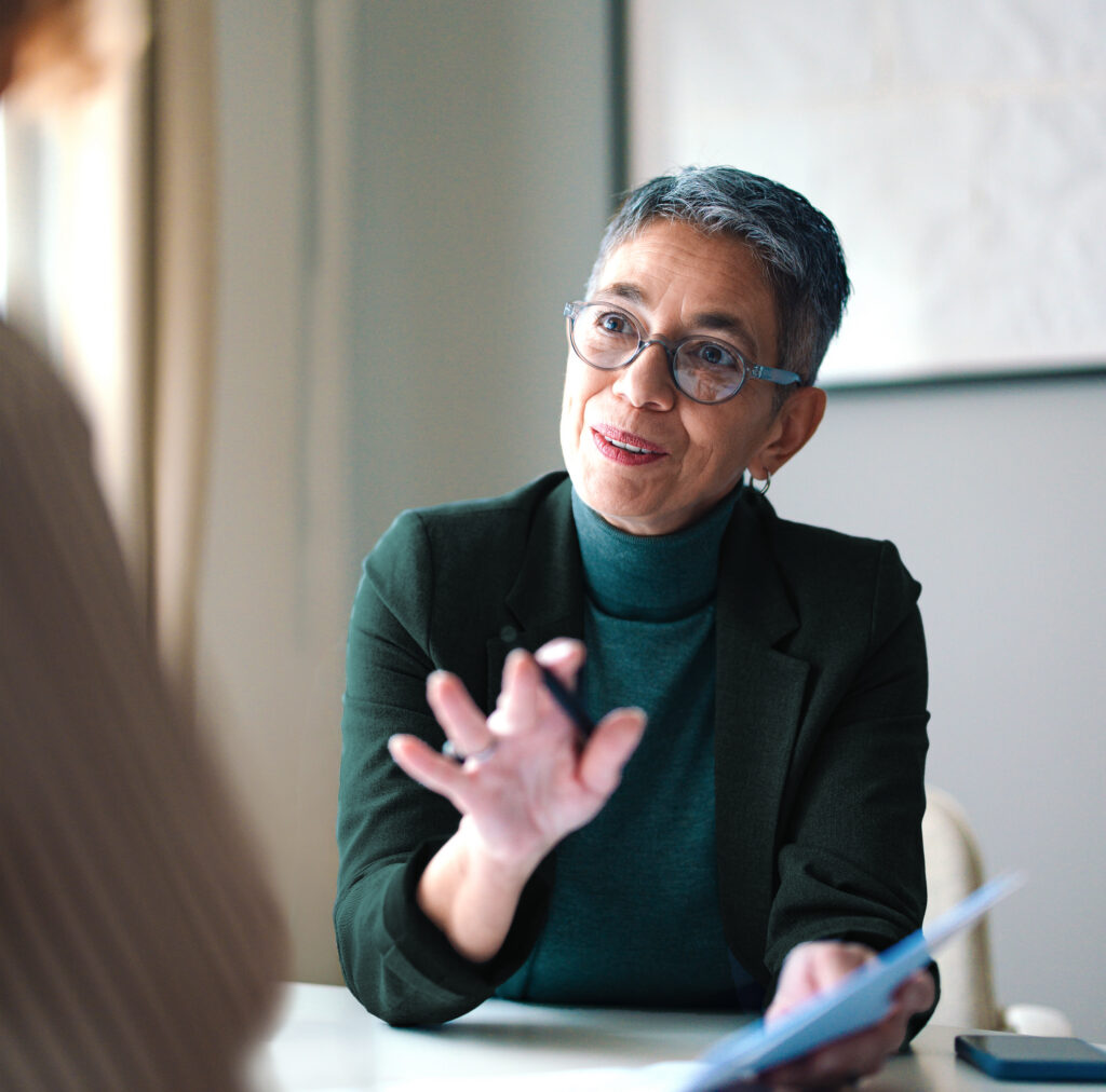 confident woman advising client across table with pen and paper in hand