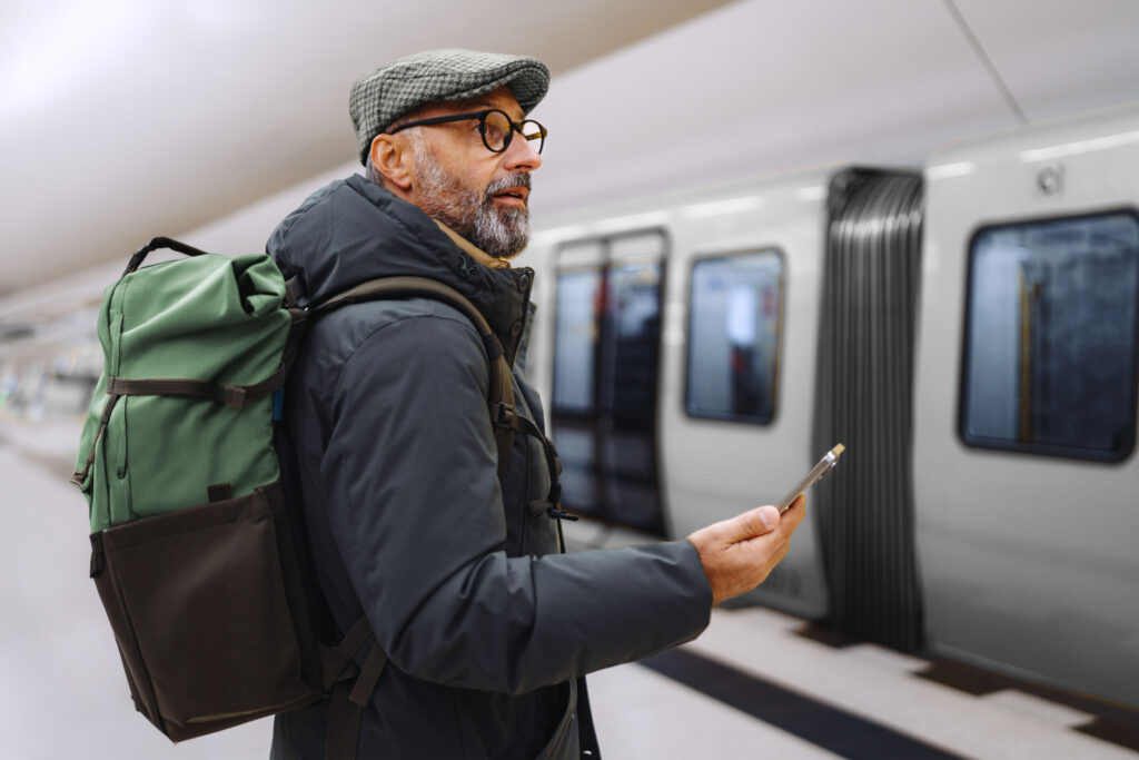 A mature man stands at a subway station, using his smartphone to sign in and preview his annuity.